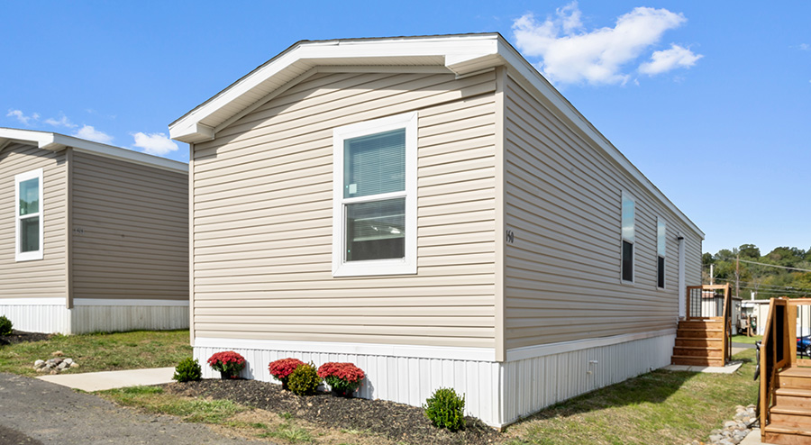 Single-story manufactured home exterior at Village Green featuring vinyl siding, front steps, and landscaped foundation
