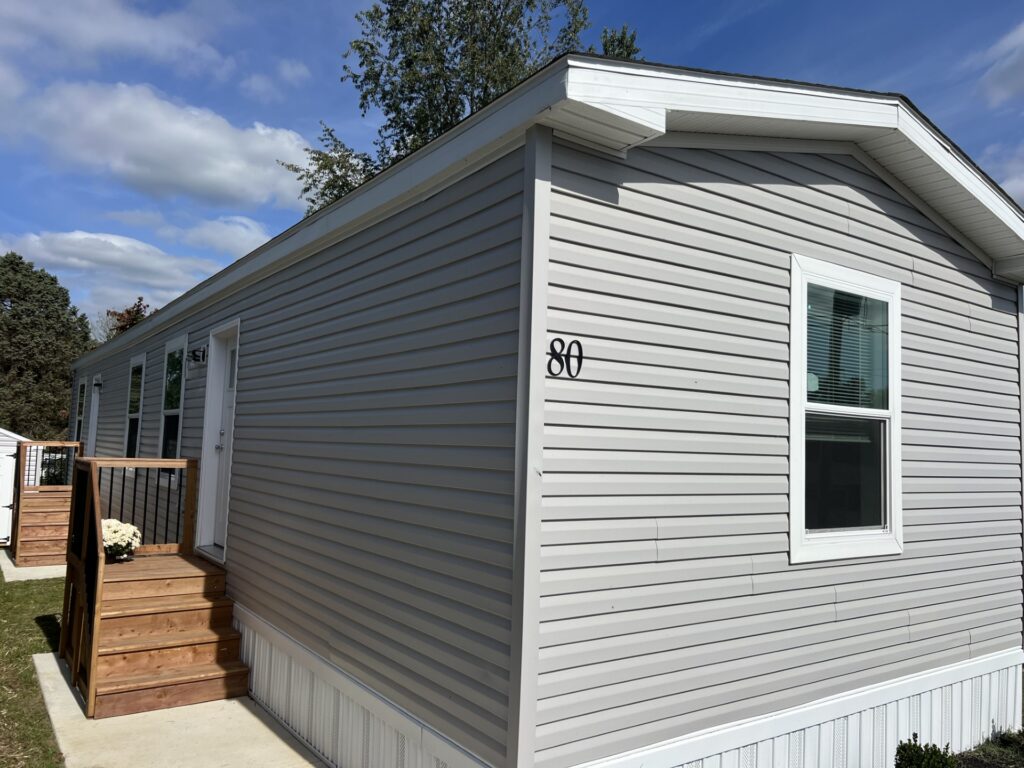 Side exterior view of a modern manufactured home with gray vinyl siding and front steps in a 55+ community in Pennsylvania